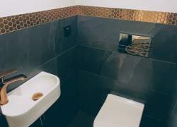 Toaleta - biała umywalka i sedes, kran nad umywalką w kolorze miedzi, na ścianie czarne i białe płytki rozdzielone złotą lamperią