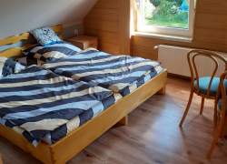 Sypialnia - drewniane łóżko, panele na podłodze, okno białe PCV, grzejnik pod oknem, wyściełane krzesło