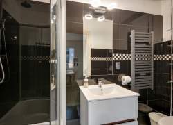 Łazienka z kabiną prysznicową, białą umywalką i lustrem, na ścianach czarne płytki