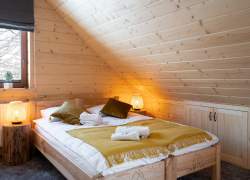 Sypialnia; na ścianach i suficie drewniana boazeria, łóżko małżeńskie drewniane; zapalone lampki nocne