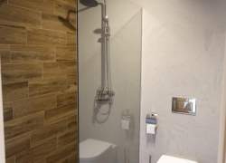 Łazienka - brązowe płytki, biały sedes, prosta szklana kabina prysznicowa