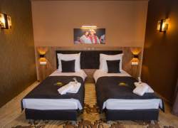 Dwa łóżka, zdjęcie pary góralskiej na ścianie, kinkiety z koronkami koniakowskimi, wzorzysta wykładzina na podłodze
