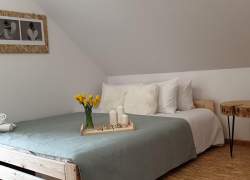 Wnętrze sypialni - przykryte szarym kocem łóżko, stolik  - plaster drewna