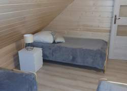 Sypialnia w jasnym drewnie, sufit pod skosem, trzy łóżka za