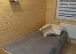 Sypialnia w jasnym drewnie, łóżko zasłane szarą kapą