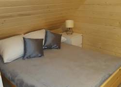 Sypialnia w jasnym drewnie, łóżko zasłane szarą kapą