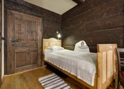 Sypialnia; ciemne ściany i drzwi, jasne drewniane łóżko z białą pościelą; przy łóżku dywanik w paski