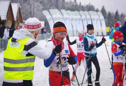 Ubrana w odblaskową kamizelkę organizatora Barbara Juroszek wręcza pamiątkowy medal uczestniczce biegu; w tle inne dziewczynki z kategorii III - IV