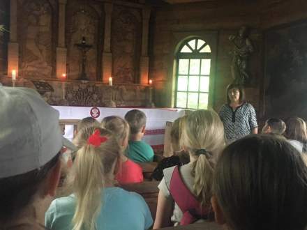 Dzieci wewnątrz drewnianej kaplicy słuchają opowieści Pani Danuty Konarzewskiej