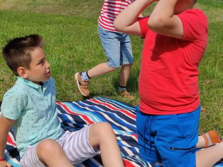 Trzech kolorowo ubranych chłopców bawi się na położonym na trawie kocu w paski