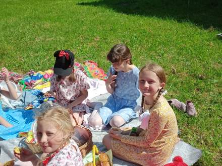 Dziewczynki siedzą przy koszykach pełnych słodkości; wkoło zielona trawa