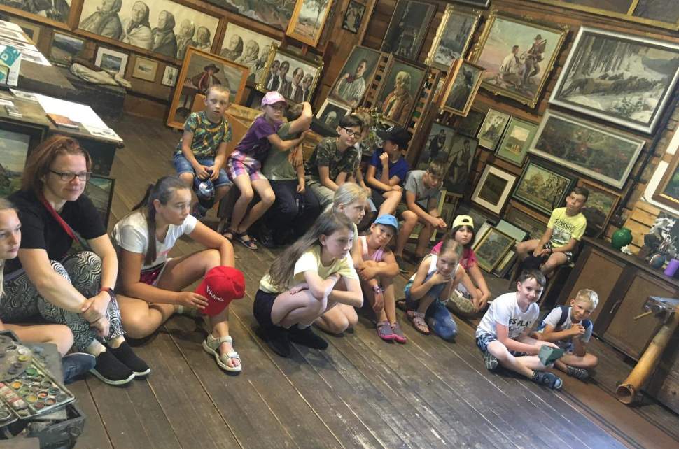 Grupa dzieci siedzących w w Muzeum Jana Wałacha i słuchających prelekcji